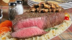 a piece of steak with mushrooms on top of it and rice, tomatoes, carrots, and cherry tomatoes