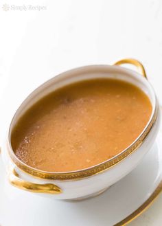 a bowl of soup on a saucer with gold trim around the rim and handles