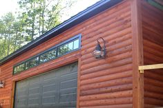 a garage with a light on the side of it in front of a log cabin