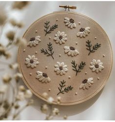 the embroidery is made with white flowers and green leaves on beige fabric, along with small brown pins