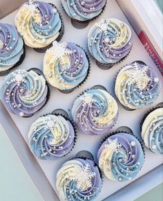 twelve cupcakes in a box with blue and white frosting on them,