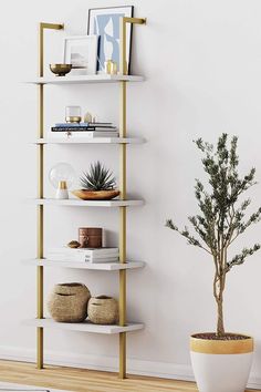 a white and gold book shelf with plants on it in front of a white wall