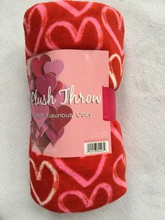 a pink and red heart shaped towel on top of a white blanket with the label plush thomas