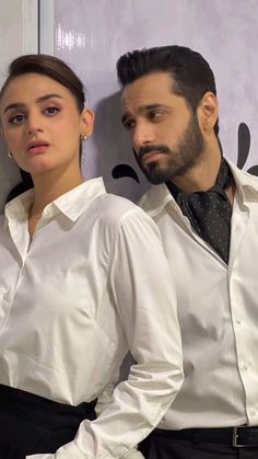 two people standing next to each other wearing white shirts and black pants, one man is looking at the camera