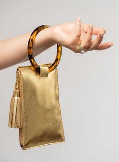 This bag is made from high-quality, super-soft metallic gold leather sourced from a premiere hide house in California. The leather is shipped to New York City, where our bags are produced by expert craftsmen and finished with a smooth zipper, leather tassel, and acrylic ring. Just big enough for all your essentials, we designed the Ring Wristlet to be your go-to bag for going out! Whether you’re heading to a cocktail party, a concert, or out on the town, slip it on your wrist so your hands are f Gold Bags With Smooth Grain For Daily Use, Gold Soft Leather Bag, Everyday Gold Leather Clutch, Gold Travel Clutch With Removable Pouch, Gold Leather Clutch, Gold Clutch With Detachable Strap For Travel, Gold Leather Clutch With Soft Leather, Gold Clutch With Removable Pouch For Daily Use, Gold Clutch With Detachable Strap For Everyday Use