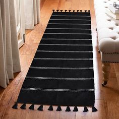 a black and white rug with tassels on the floor next to a couch