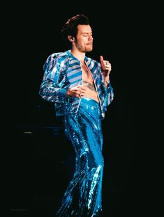 a man in blue sequins is standing on stage with his hands up to his chest