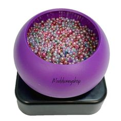 a purple bowl filled with lots of beads on top of a black base and bottom