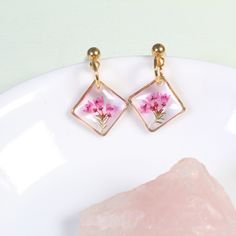 These dainty, handmade resin pressed flower earrings feature real pink heather flowers in a gold or silver diamond-oriented square setting. Real flowers are carefully preserved, clipped, then cured in several layers of resin. Small and lightweight, classy enough for a wildflower wedding, but tasteful enough that they're perfect for everyday wear.  Dimensions: From stud to bottom of earring - 1 inch Width - just over a 1/2 inch Ball studs are hypoallergenic and each pair comes with a steel and si Silver Pressed Flowers Drop Earrings, Delicate Pressed Flower Jewelry, Botanical Jewelry With Pressed Flowers, Botanical Drop Earrings With Birth Flower, Rose Gold Pressed Flower Earrings, Dainty Pink Gold Flower Jewelry, Botanical Birth Flower Drop Earrings, Elegant Pink Jewelry With Pressed Flowers, Elegant Pink Pressed Flowers Jewelry