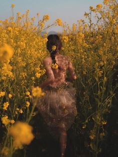 a woman walking through a field full of yellow flowers