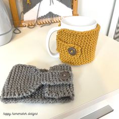 two knitted mittens sitting on top of a table next to a coffee mug