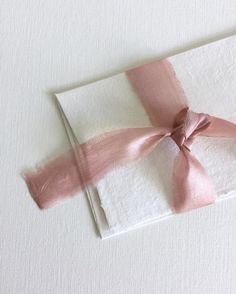 a napkin with a pink ribbon tied around it on top of a white table cloth