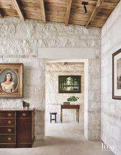 a painting hangs on the wall next to a dresser and table in a stone walled room