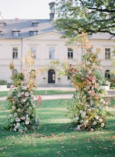 three tall vases filled with flowers in front of a large white building on the grass