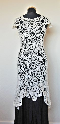 a white crochet dress on a mannequin stand next to a wall