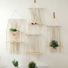 three macrame hangings on the wall above a table with potted plants