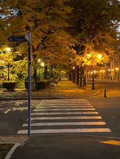 an empty street at night with lights on and trees lining the road in front of it