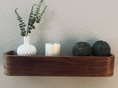 a wooden shelf with two vases and candles on it next to a white wall