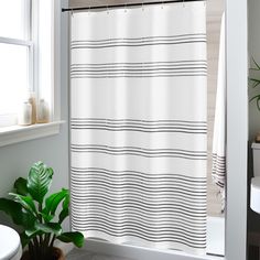 a bathroom with a white shower curtain next to a potted plant on the floor