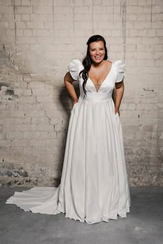 a woman standing in front of a brick wall wearing a white dress with ruffle sleeves