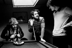 three men standing around a pool table with one holding a cue in his other hand