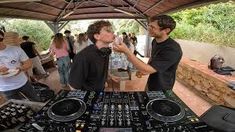 two men standing next to each other in front of dj's at an outdoor event