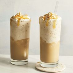 two glasses filled with ice cream and caramel on top of a white table next to each other