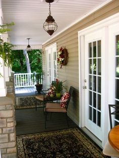 a porch with chairs, table and potted plants on the front door sill