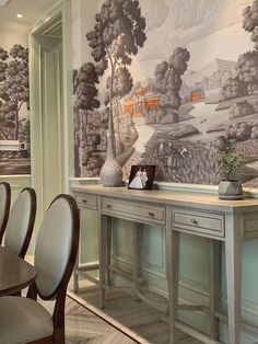 a dining room table with chairs and a wall mural behind it that has a landscape on the wall