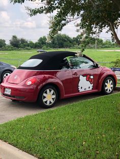 a hello kitty convertible parked on the side of a road next to a tree and grass field