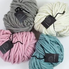 four skeins of yarn in different colors on a white background with a black tag