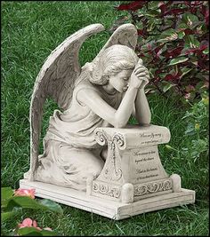 an angel statue sitting in the grass with his hands clasped to his face and praying