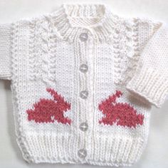 a white knitted sweater with red hearts on the front and back, sitting on top of a table