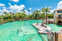 people are swimming in the water at an outdoor pool with palm trees and blue skies