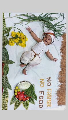 a baby laying on top of a white blanket next to flowers and fruit in bowls