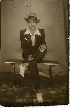 an old black and white photo of a woman in a suit sitting on a bench