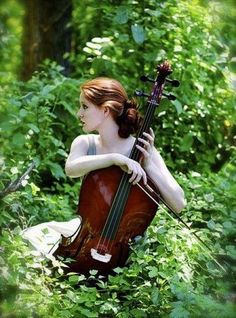 a woman sitting in the grass playing a cello