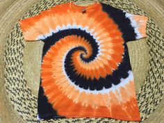 an orange and black tie - dyed t - shirt sitting on top of a straw hat