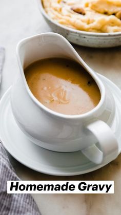 a cup of soup on a saucer next to a plate with pies in the background