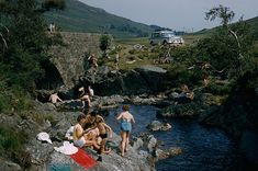 some people are sitting on rocks by the water and one person is swimming in the river