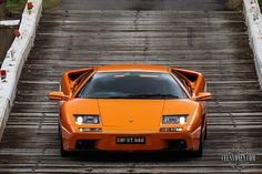 an orange sports car is parked on a wooden bridge over the water and it's doors open