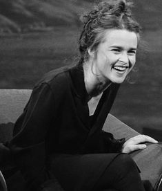 a black and white photo of a woman sitting on a couch smiling at the camera