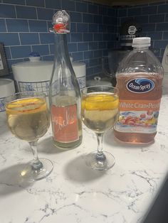 two glasses filled with liquid sitting on top of a counter next to a bottle of water