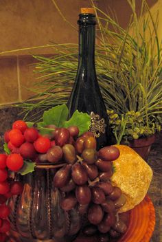 a plate with grapes and bread on it next to a wine bottle, potted plant and other items