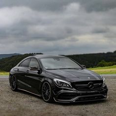 a black mercedes cla is parked on the side of the road with dark clouds in the background