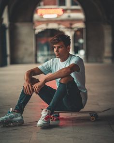 a young man sitting on the ground with his skateboard in front of him,