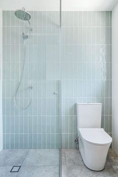 a white toilet sitting in a bathroom next to a walk in glass shower stall and tiled walls