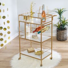 a gold bar cart with wine bottles and glasses on it in a living room next to a potted plant