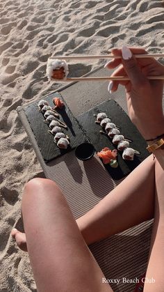 a woman sitting in the sand with chopsticks and sushi on her lap