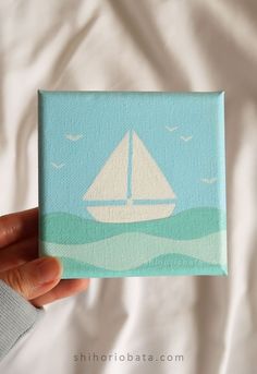 a person holding up a small painting with a sailboat on it